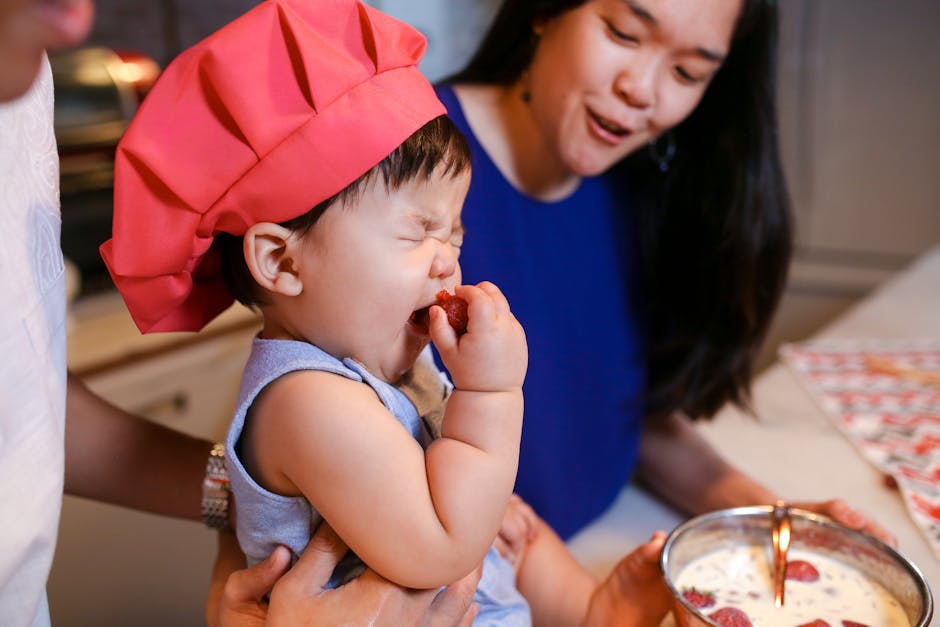 Baby in chef hat enjoys strawberries with family in kitchen. Perfect for depicting family cooking fun. (Photo : RDNE Stock project / Pexels)